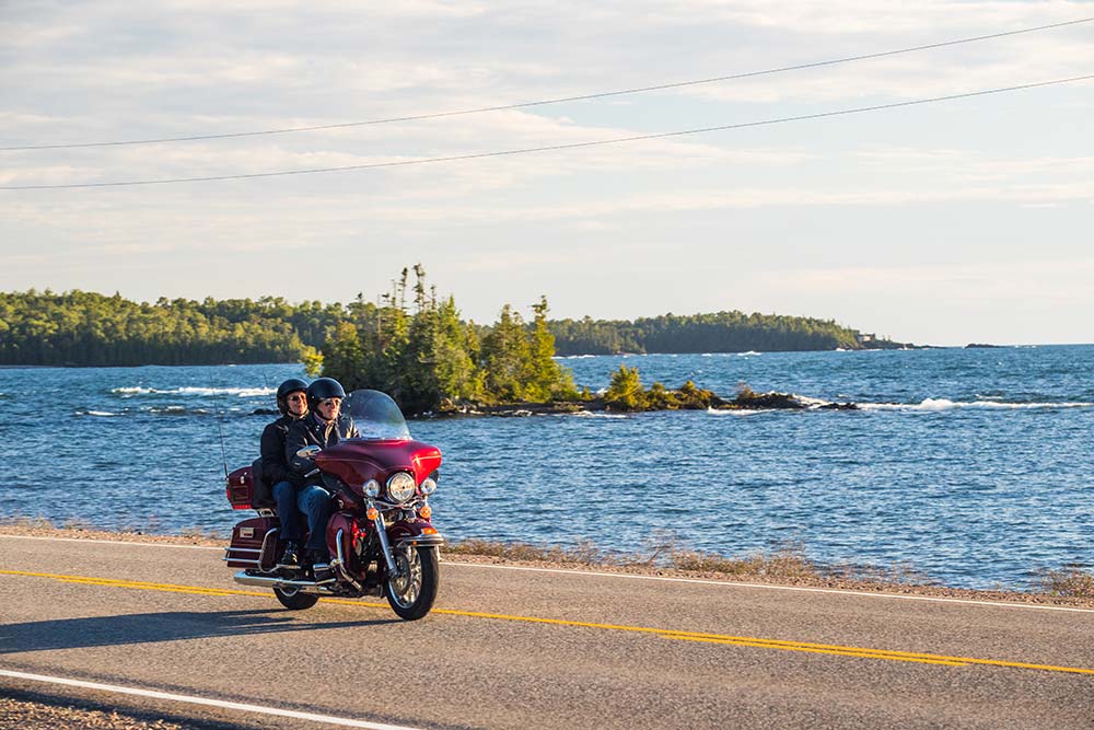 couple riding lake superior road by motorcycle